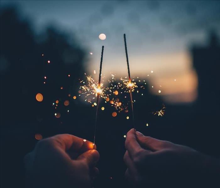 Close up of two hands holding lit sparklers with moon in background