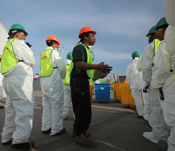A group of SERVPRO technicians dressed in protective equipment while a team leader addresses them